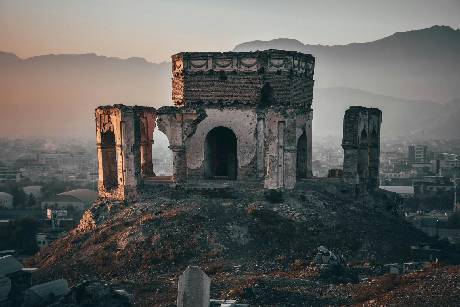 Aged ruins of King Nader Shah's tomb with a backdrop of Kabul city at dusk, displaying rich history.